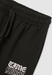 Czarne spodnie dresowe z elastycznym pasem, wyposażone w sznurek i biały nadruk z tekstem „TIMELESS” na lewej udzie.