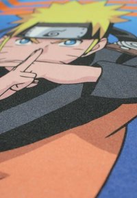 Illustration représentant un personnage aux cheveux blonds en pointes, aux yeux bleus, portant un bandeau. Le personnage est vêtu d'une tenue noire et orange, réalisant un signe de la main.