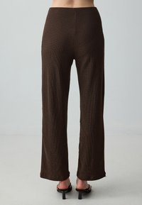 Pantalons marron texturés avec une coupe large, dotés d'une taille haute et d'un léger effet côtelé, associés à des chaussures noires à bout ouvert.