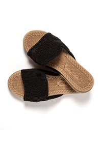 Black slide sandals with textured fabric straps featuring circular patterns, and a molded tan rubber sole with a geometric design.