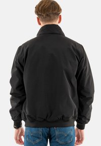 Zwarte windbreaker jas met een hoge kraag, elastische manchetten en tailleband, met een gladde textuur en een eenvoudig, onopgemaakt ontwerp.
