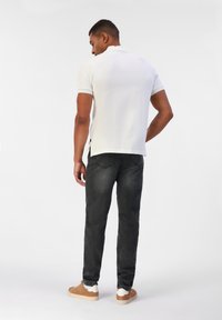 Polo blanc à manches courtes avec un ourlet droit, associé à un jean gris foncé et des baskets beiges avec des semelles blanches, doté d'un tissu texturé.