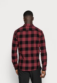 Czerwona i czarna koszula w kratę na guziki, z długimi rękawami, kołnierzykiem i zaokrąglonym dołem. Materiał ma fakturę o miękkim, tkanym wyglądzie.