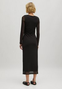 Schwarzes langärmliges Kleid aus dehnbarem Mesh-Stoff, mit einer figurbetonten Silhouette, hohem Kragen und durchsichtigen Ärmeln in knöchellanger Ausführung.