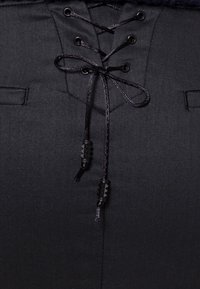 Vêtement noir avec un détail de laçage à l'avant présentant des cordons noirs enfilés à travers des œillets métalliques, noués en un nœud avec des extrémités de cordon texturées.