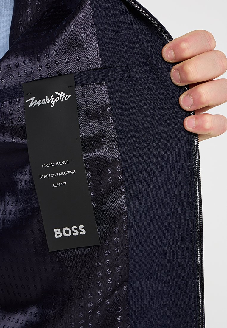 Das Innere der Marinejacke ist aus glattem Stoff mit einem subtilen Muster. Das Etikett trägt die Aufschrift "Marzotto" und spezifiziert "Italienischer Stoff", "Stretch-Schneiderkunst" und "Slim Fit."