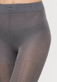 Sivé legíny vyrobené z hladkého, elastického materiálu, s textúrovaným vzorom na dolnej časti nohy a rebrovaným pásom.