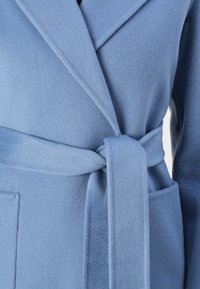 Jasnoniebieski płaszcz z mieszanki wełny z klapami, paskiem do wiązania i bocznymi kieszeniami. Miękka struktura i szczotkowane wykończenie z dopasowaną sylwetką.