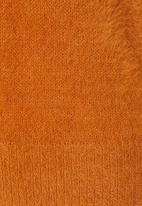 Primo piano di un morbido e peloso tessuto di maglia arancione con una texture a coste lungo il bordo inferiore.