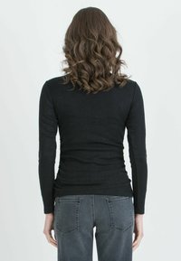 Black long-sleeve ribbed top, fitted design, made from textured fabric, paired with gray denim jeans.