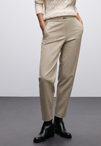 Pantalons beige cintrés avec poches avant et taille élastique, associés à des bottines noires, présentés sur un fond neutre.