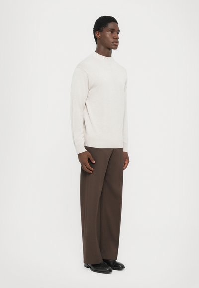 Light gray sweater with a high neckline, ribbed cuffs, and hem, paired with dark brown wide-leg trousers and black shoes.