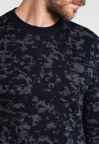 Marineblauer Pullover mit strukturiertem, abstraktem grauem Muster, Rundhalsausschnitt und gerippten Bündchen, aus weichem Strickmaterial gefertigt.