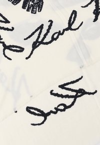 Tissu blanc avec du texte et des motifs noirs de style manuscrit. Le matériau a une texture douce avec des bords effilochés.