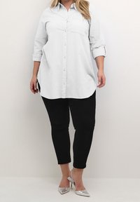 Lysegrå langærmet skjorte med knapper foran og en brystlomme, kombineret med sorte smalle bukser og sølvfarvede højhælede sko.