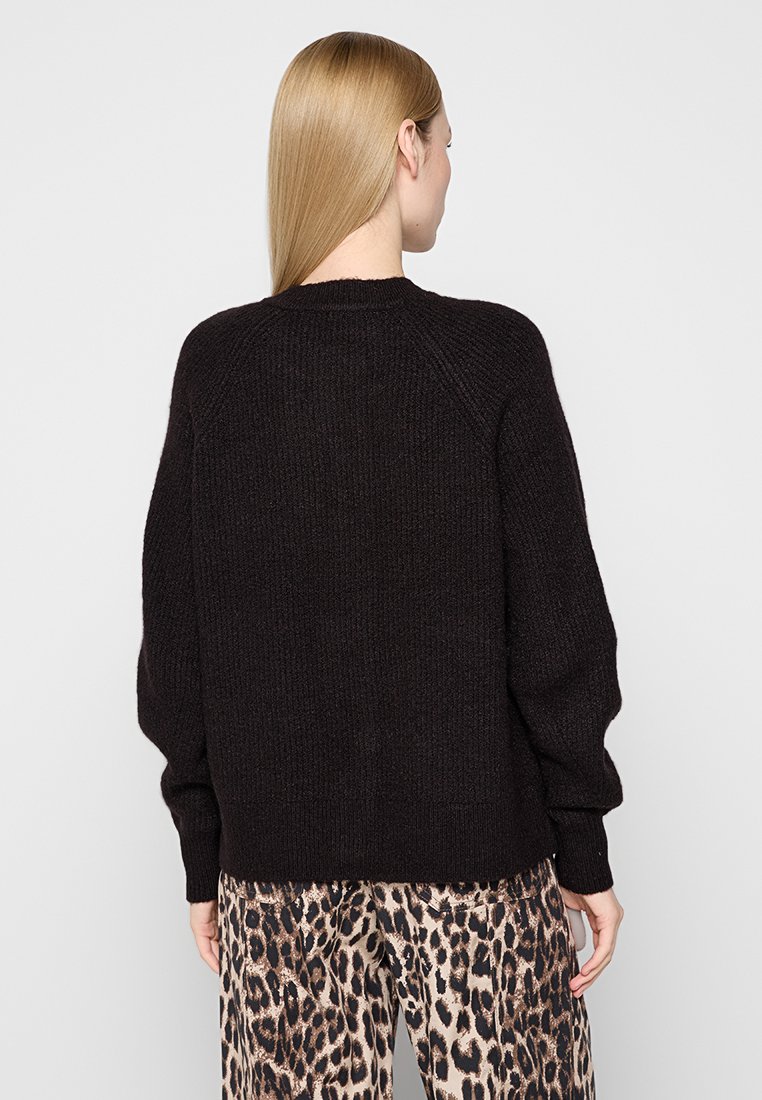 Schwarzer, gestrickter Pullover mit Rundhalsausschnitt, lockerer Passform und Raglanärmeln, kombiniert mit gemusterten Hosen im Leopardenprint.