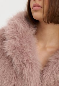 Cuello de piel sintética rosa con textura suave y esponjosa, enmarcando la zona del cuello. Presenta un aspecto profundo y mullido con un brillo natural.