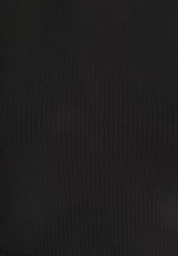 Gros plan sur un tissu noir côtelé avec des lignes texturées verticales, montrant le motif de tricot détaillé et l'élasticité du tissu.