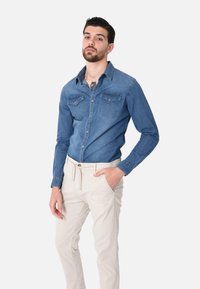 Camicia di denim blu con due tasche sul petto, colletto con bottoni e maniche lunghe, abbinata a pantaloni a sigaretta color crema.
