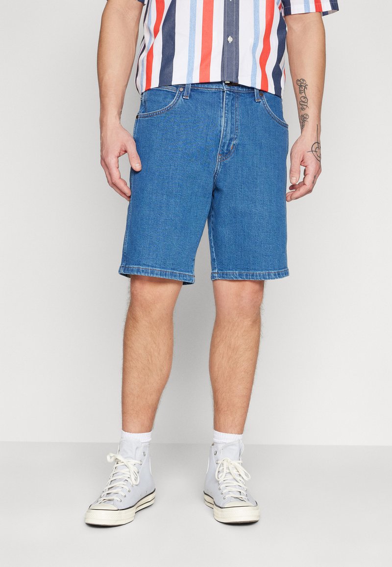 Shorts de mezclilla azul con corte recto, diseño de cinco bolsillos y dobladillos enrollados, combinados con zapatillas altas de color azul claro.
