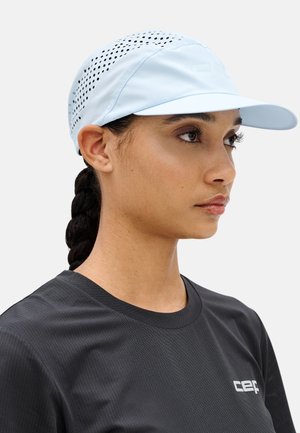 Woman with braided hair wearing a light blue perforated cap and a black crew-neck athletic shirt facing right.
