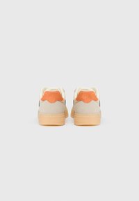 Sko med beige suede overdel, oransje hæltab og lys brun gummisåle, med rund tupp og kontrasterende svarte detaljer.