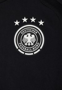 Logo de l'équipe nationale allemande de football avec quatre étoiles au-dessus d'un fond de maillot noir.