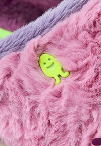 Produit en fausse fourrure avec des textures vibrantes rose et violet, comprenant un petit personnage vert souriant intégré dans la zone rose.