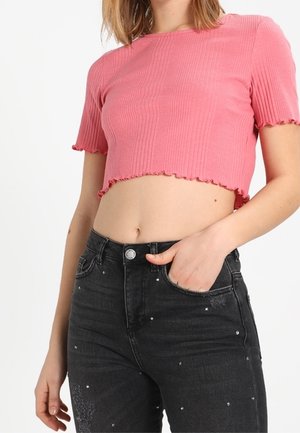 Różowy, prążkowany krótki top z krótkimi rękawami i falowanym dołem, zestawiony z czarnymi, wysokim stanem jeansami ozdobionymi srebrnymi ćwiekami.