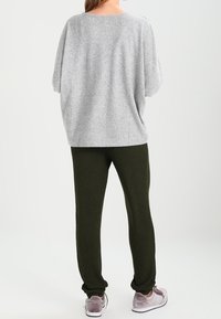 Szary, oversize sweter z krótkimi rękawami, w połączeniu z zielonymi dresami i jasnofioletowymi trampkami. Miękka tkanina z luźnym krojem.