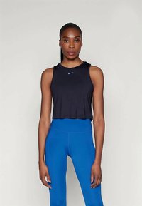 Svart ermeløs crop topp med Nike-logo, kombinert med høyt liv blå leggings. Glatt stoff, tettsittende design og minimal detaljering.