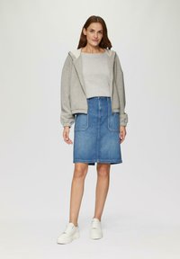 Haut à zip gris, top gris clair, jupe en denim bleu avec deux poches avant, longueur au genou, associée à des baskets blanches.
