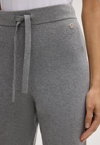 Grijze joggingbroek gemaakt van gestructureerde stof, met een geribde tailleband, verstelbaar koord en een klein rond metallic logo-detail.