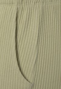 Khakifarbenes, geripptes Baumwollgewebe mit ausgeprägten vertikalen Linien, ausgestattet mit einer Seitentasche, weicher Textur und sorgfältigen Nähdetails.