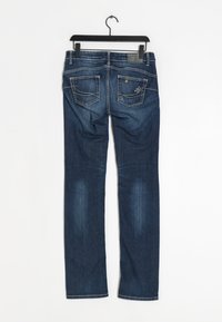 Mörkblå denimjeans med slim fit. Har dekorativt stygn på bakfickorna och en läderetikett vid midjan. Hänger från en svart krok.