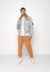 Light gray bomber jacket with a brown fur collar, zip closure, and multiple pockets, paired with orange joggers and white sneakers.