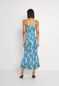 Robe maxi en tissu léger et respirant, ornée d'un motif ondulé bleu et vert, avec des bretelles fines ajustables et une silhouette près du corps.