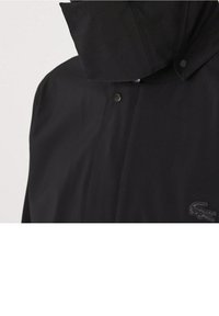 Černá voděodolná bunda s vysokým límcem, cvakacími uzávěry a texturovanou tkaninou. Logo Lacoste v černé barvě na dolní pravé straně.