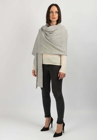 Lysegrå uldomslag draperet over en cremefarvet sweater, parret med mørke stramme jeans og sorte spidse hæle. Glat tekstur, minimalistisk design.