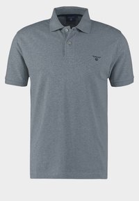 Polo gris en tissu mélange de coton. Il comporte un col, des manches courtes, et un petit logo brodé sur la partie gauche de la poitrine.