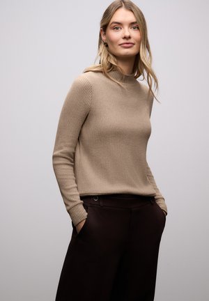 Beige geribbelde top met lange mouwen, een hoge hals en een getailleerde pasvorm, gecombineerd met donkerbruine broek met zijzakken en een knoopdetail.