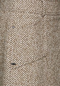 Tissu en chevrons brun et blanc avec une finition texturée ; présente un bouton argenté et une petite étiquette de logo sur le côté.