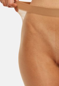 Collant trasparenti color nudo con una texture liscia e un elastico in vita, leggermente tirati per mostrare la vestibilità e i dettagli del design.