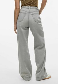 Jeans de pierna ancha gris claro con una cintura alta, dos bolsillos traseros y un dobladillo doblado. Hechos de denim, la tela tiene una textura suave y lisa.