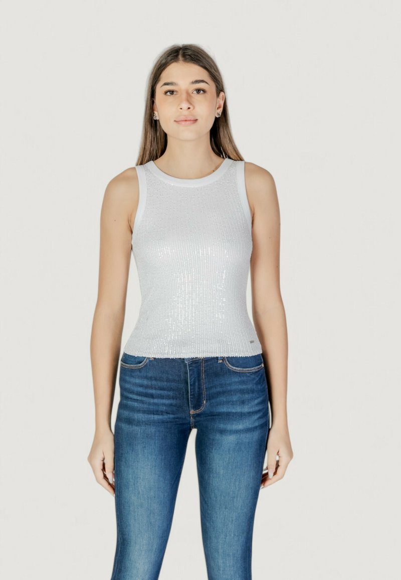 Top bianco senza maniche con un motivo di paillettes textured, abbinato a jeans attillati blu scuro. Design minimalista che mette in risalto la brillantezza del top.