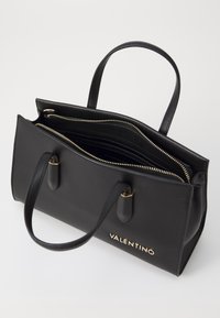 Černá kožená kabelka se zlatým kováním, dvojitými rukojeťmi a několika přihrádkami se zipovými uzávěry. Na přední straně je vyraženo logo "VALENTINO".