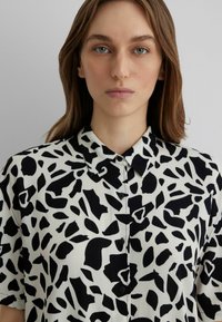 Short-sleeve shirt in a white fabric with a black abstract pattern. Features a button-up front and a classic collar.