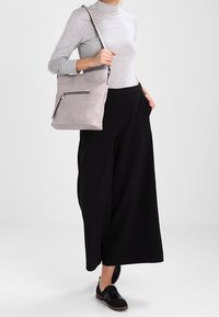 Grå långärmad topp, svarta vida byxor och en ljusgrå axelväska med en dragkedja och en slät yta. Svarta snörskor.