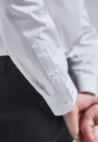 Witte overhemd met een gladde textuur, gekleed met een puntige manchet met twee knopen, en gecombineerd met donkere broek.