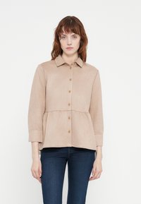 Light beige button-up shirt with a peplum waist, long sleeves, and a collar. Made from soft fabric with a smooth texture.